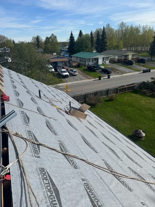 A metal roof is being installed on a single-family home in a rural area with lush greenery.