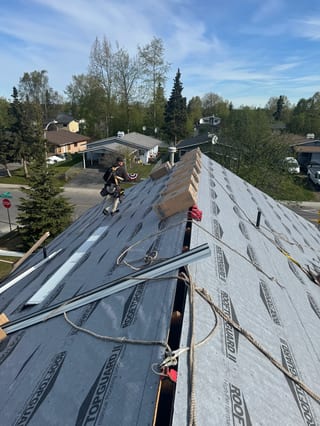 Metal roof underlayment installed on a house with a blue sky and lush greenery in the background.