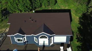 Aerial view of a finished brown metal roof on a single-family ranch-style home in a forested rural setting
