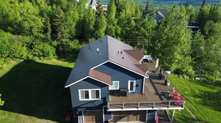 A modern house with a brown metal roof and dark blue siding, surrounded by trees and greenery