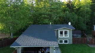 A modern style house with a grey metal roof and white trim in a forested area with lush greenery
