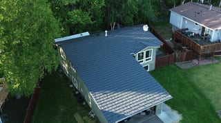 Aerial view of a finished metal roof on a ranch style home in a forested rural setting.