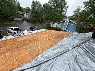 A metal roof under construction in a suburban area with lush greenery and an overcast sky.