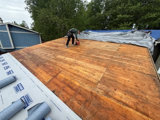 A craftsman-style home with a brown metal roof under construction in a wooded area.
