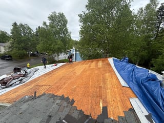 A metal roof under installation on a single-family home in a forested, rural area.