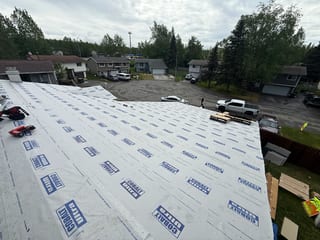 A modern metal roof is being installed on a single-family home in an urban forested setting.