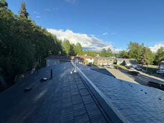 A finished metal roof in a ranch style home with lush greenery and a blue sky