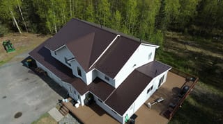 Aerial view of a modern single-family home with a brown metal roof and a forested, rural setting