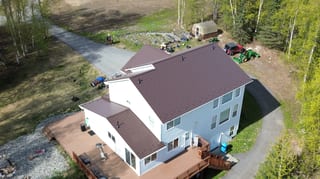 Metal roof with a dark brown finish on a modern single-family home in a forested rural area