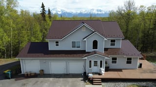 A modern house with a brown metal roof in a forested mountain setting
