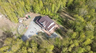 Aerial view of a ranch-style home with a brown metal roof under construction in a wooded area