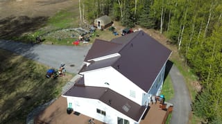 A white ranch-style home with a brown metal roof, situated in a forested rural area.