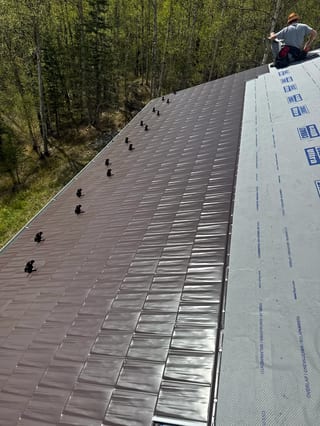 A metal roof under construction in a forested, rural area.