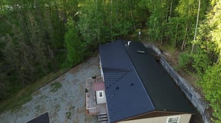 Aerial view of a metal roof on a single-family home in a forested rural area.