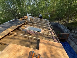 A cottage with a metal roof under construction in a forested mountain area.