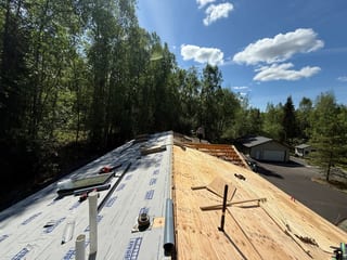 A modern-style home with a metal roof under construction in a forested rural area.