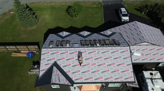 A modern metal roof is being installed on a house with black trim and siding