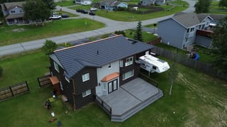 A two-story ranch-style home with a black metal roof and white siding