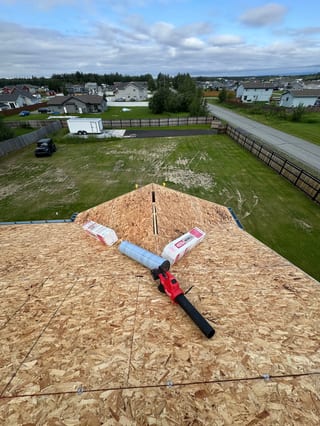 A metal roof in progress, with exposed decking and underlayment, on a suburban home with a brown roof