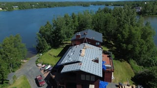 A modern single-family home with a gray metal roof overlooking a lake and forest.