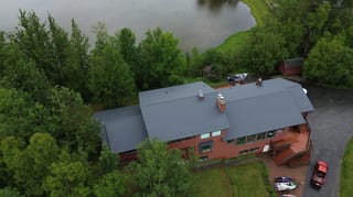 A red ranch-style house with a grey metal roof and a lake in the background
