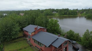 Aerial view of a red modern home with a grey metal roof overlooking a lake.