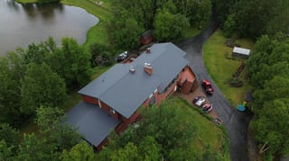 A ranch-style home with a red metal roof, set against a backdrop of lush greenery and a serene lakeside setting.