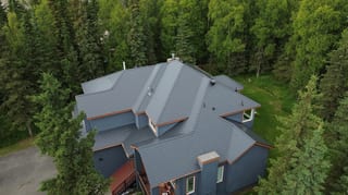 Aerial view of a modern house with a grey metal roof surrounded by lush greenery