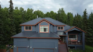 A large house with a grey roof and brown trim, set against a backdrop of trees.