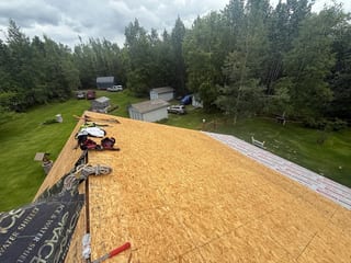 A metal roof under construction on a house in a wooded area.