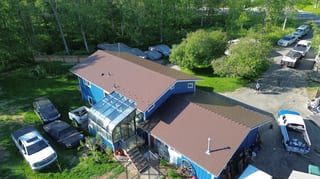 Aerial view of a blue ranch-style home with a brown metal roof and a driveway with several vehicles