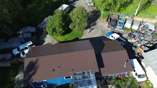 A brown metal roof on a single-family ranch style home in a forested rural area