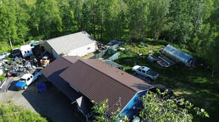 Aerial view of a house with a brown metal roof, surrounded by lush greenery