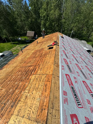 A metal roof is being installed on a house in a forested area.