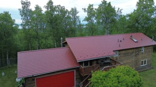 A modern house with a red metal roof in a forested mountain setting
