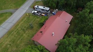 A ranch style house with a red metal roof and a white RV parked in the driveway.