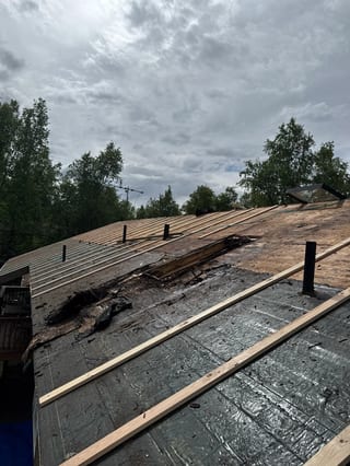 A partially installed metal roof on a house in a wooded rural setting.