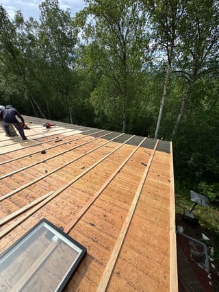 A metal roof is being installed on a house in a forested area.