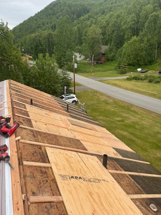 A metal roof being installed on a house in a forested area with lush greenery and overcast sky