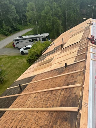 A metal roof under construction with snow guards and ridge cap in a forested rural area