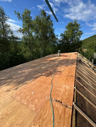 A new metal roof is being installed on a modern single-family home in a forested mountain setting