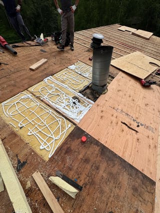 A modern metal roof being installed on a single-family home in a forested mountain setting.