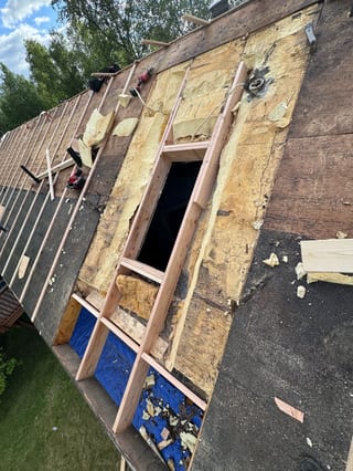 A metal roof being installed on a house in a forested urban area with lush greenery.