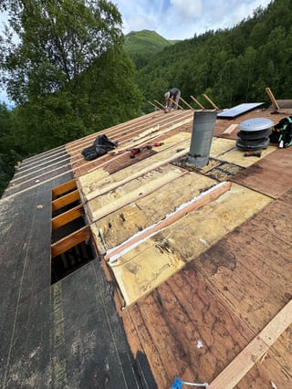 A metal roof under construction in a forested mountain setting.
