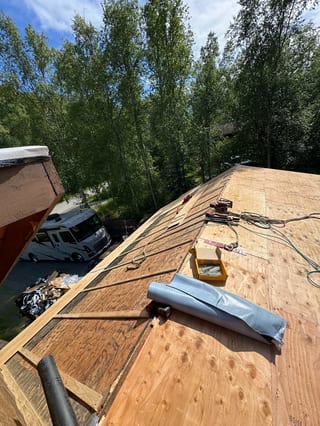 A metal roof being installed on a ranch-style single-family home in a forested mountain setting.