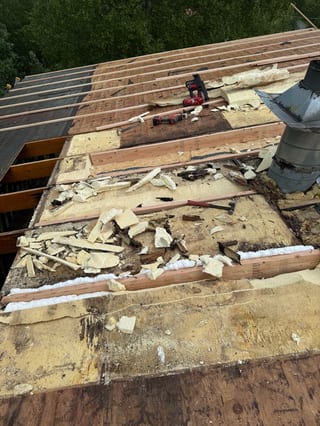 A partially completed metal roof on a forested single-family home