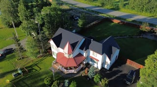 Aerial view of a modern single-family home with a finished metal roof in a rural forested setting.
