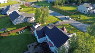 A ranch-style house with a black metal roof in a wooded, rural area