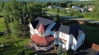 Aerial view of a white Victorian home with a black metal roof and red trim