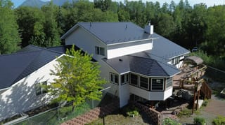 Aerial view of a modern, white single-family home with a dark grey metal roof and snow guards.